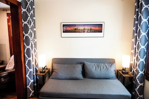 A hotel room with a bed, two bedside tables with lamps, a framed cityscape picture on the wall, patterned curtains, and a wooden door. - Newly Remodeled Riverfront Cottage (Rockford)