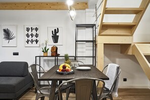 A dining area with a wooden table, chairs, and a fruit platter. There is a sofa and a staircase in the background. - Planell · BOLSA 2H - Two Bedroom Apartment, Sleeps 4 (Barcelona)