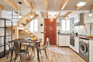 A compact kitchen with a dining area, wooden beams, and a built-in washing machine. - Planell · BOLSA 2H - Two Bedroom Apartment, Sleeps 4 (Barcelona)
