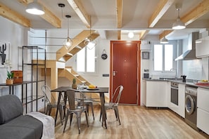 A compact kitchen with a wooden staircase, a dining area with chairs, and a sofa. - Planell · BOLSA 2H - Two Bedroom Apartment, Sleeps 4 (Barcelona)