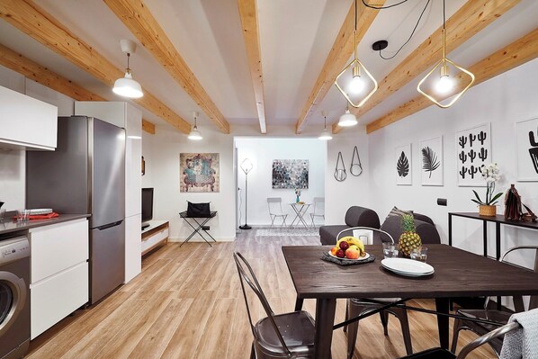 A modern kitchen with stainless steel appliances, wooden beams, and a dining area with a table set for two. - Planell · BOLSA 2H - Two Bedroom Apartment, Sleeps 4 (Barcelona)