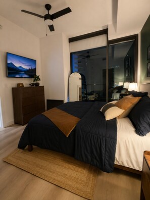 Ein modernes Schlafzimmer mit Bett, Fernseher, Deckenventilator und Blick auf die Stadt durch ein großes Fenster.