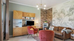 Ein Wohnzimmer mit Sofa, Sessel, Fernseher und Kamin.