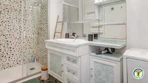 Ein Badezimmer mit weißem Waschbecken, einem großen Spiegel, einer Duschkabine mit Terrazzowand und einer Toilette.