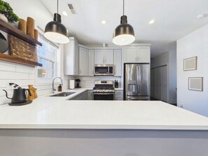 Una cocina moderna con armarios blancos, electrodomésticos de acero inoxidable e iluminación colgante.