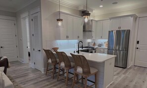 A modern kitchen with white cabinets, a stainless steel refrigerator, and a central island with bar stools. - Dune & Pine - 4 Ensuite Bedrooms -3 King Beds, Community Pool, Bikes + Beach (Santa Rosa Beach)