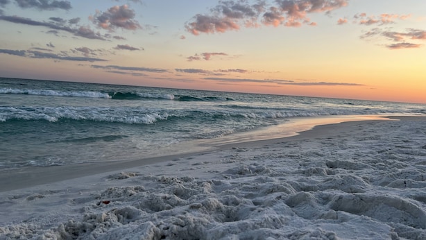 Ein Strand mit Wellen, blauem Himmel und Sonnenuntergang.
