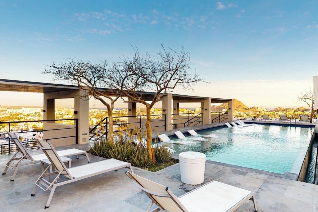 A rooftop pool with lounge chairs, a tree, and a view of the city.