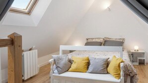 A bedroom with a sloped ceiling, a white bed, and a skylight.