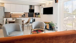 A modern kitchen with white cabinets, a flat-screen TV, and a dining area with a table and chairs.