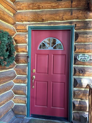 A red door with a glass window above it, a welcome sign, and a wreath on the left. - Log Cabin Bliss ~ Game Room ~ Pets ~ WiFi (Carnelian Bay)
