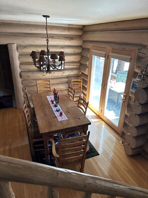 A log cabin interior with a wooden dining table, chairs, a chandelier, and a view through a glass door. - Log Cabin Bliss ~ Game Room ~ Pets ~ WiFi (Carnelian Bay)