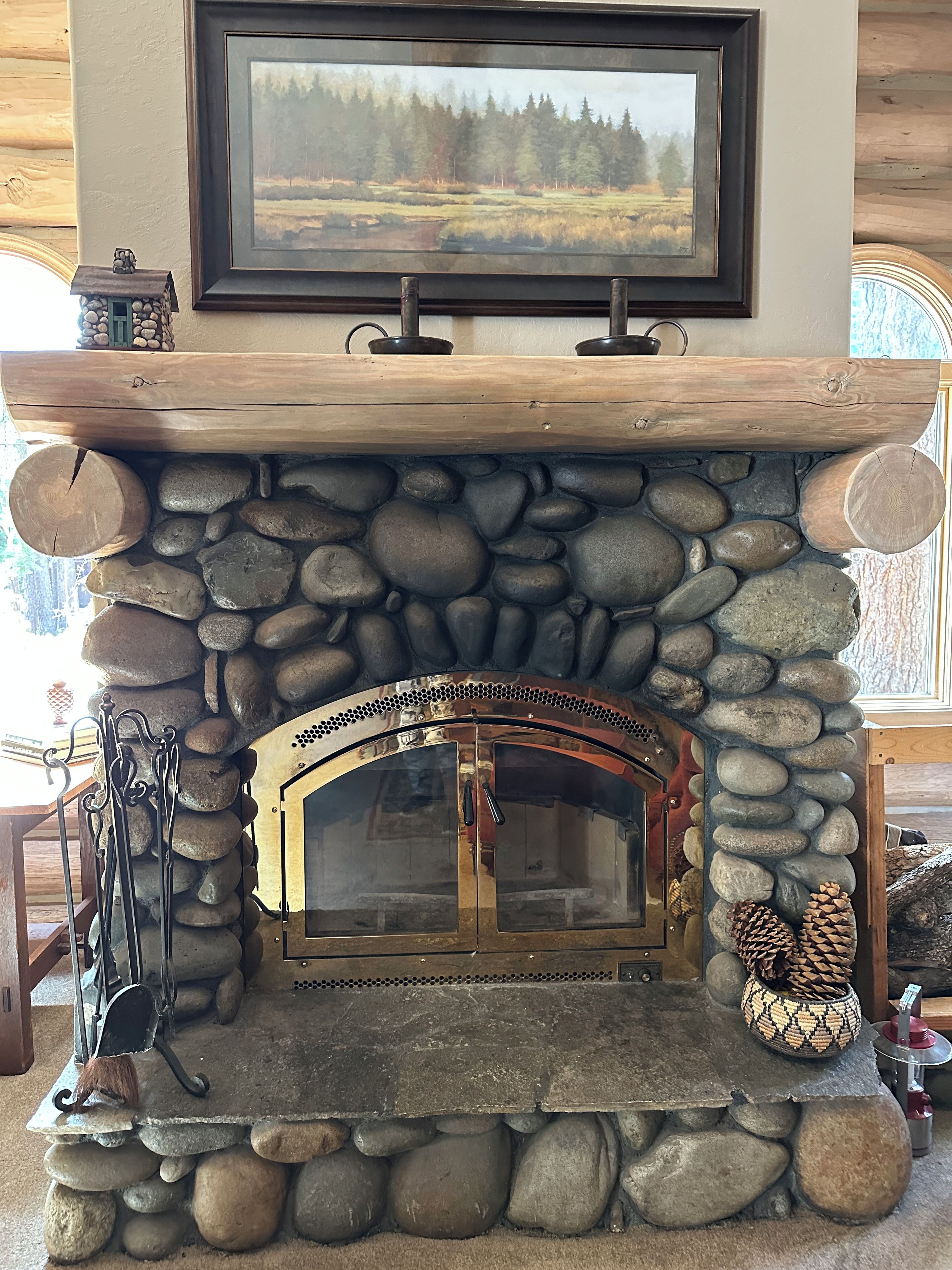 A stone fireplace with a wooden mantel, a framed picture above it, and a rustic decor including a small house model and pinecones.