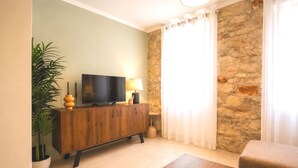 Een woonkamer met een televisie, een houten kast, een potplant en een stenen muur.