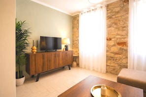 Ein Wohnzimmer mit Fernseher, Holzschrank, Topfpflanze und Steinwand.