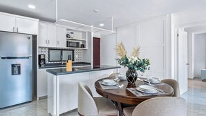 A modern kitchen with white cabinets, a central island, and a dining area with a round table and chairs. - Morgan Residences 508a at Boutique Hotel With Pool, Gym, Spa (Cabo San Lucas)