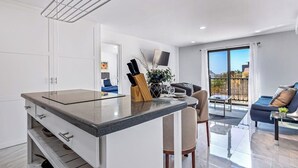 A modern kitchen with a central island, a dining area with a sofa and table, and a balcony with a view. - Morgan Residences 508a at Boutique Hotel With Pool, Gym, Spa (Cabo San Lucas)