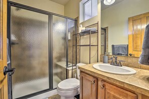 Ein Badezimmer mit Duschabtrennung aus Glas, Toilette, Waschbecken mit Spiegel und Holzschränken.