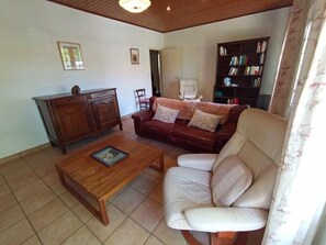 Ein Wohnzimmer mit Couch in Rot, weißem Sessel, Bücherregal und Holztisch sowie Holzschrank.