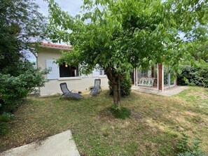 Ein Haus mit Garten, zwei Liegestühlen, einem Baum und einem kleinen Bauwerk mit Glasveranda.