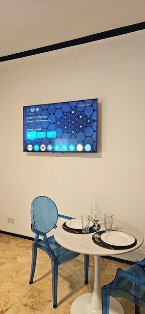 A modern interior with a mounted TV displaying a Google TV interface, a round table with a white base and blue chairs, and a clean, minimalist design. - Blue Montevideo (Buenos Aires)
