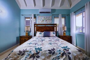 Ein Schlafzimmer mit einem blumigen Überwurf auf dem Bett, einem hölzernen Kopfteil, zwei Nachttischen mit Lampen und einem Fenster mit Vorhängen.