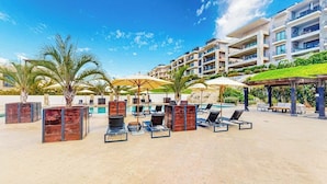 Een resort met terrasjes, palmbomen, een zwembad en moderne gebouwen op de achtergrond.