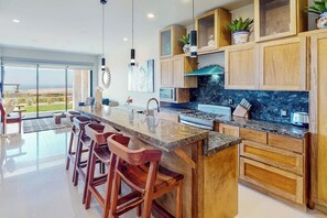 A modern kitchen with a large island, wooden cabinets, and a view to the outdoors. - Ground-floor Condo With Ocean View, Pool, Gym, Hot Tub, & Washer/dryer (Cabo San Lucas)