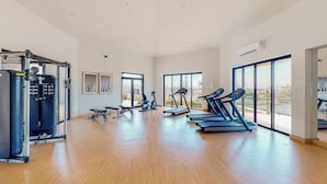 Een ruime fitnessruimte met cardioapparatuur, krachttoestellen en grote ramen.