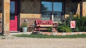 A building with a red door, stone walls, a bench, and a small garden area. - Cozy 2-bedroom apartment is amazing  peaceful some call it a gem. (Kempner)