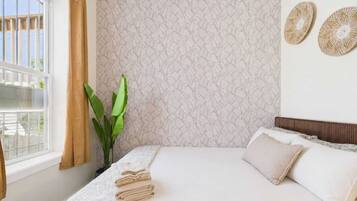 A bedroom with a bed, a window with curtains, a plant, and a textured wall.