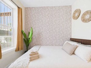 A bedroom with a bed, a window with curtains, a plant, and a textured wall.