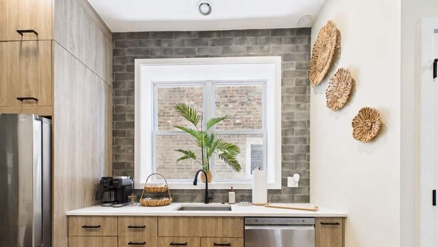 A modern kitchen with wooden cabinets, a stainless steel dishwasher, and a window with a view of a brick wall.