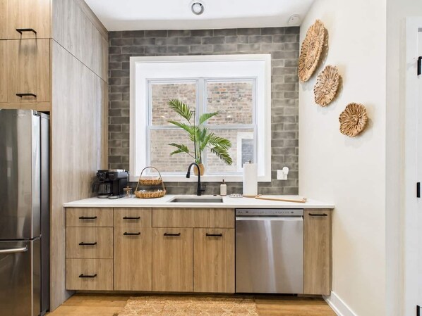 Une cuisine moderne avec des meubles en bois, un lave-vaisselle en acier inoxydable et une fenêtre donnant sur un mur de briques.