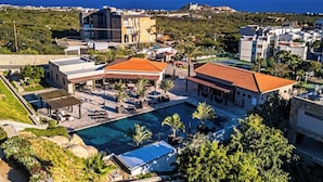 A resort with a swimming pool, multiple buildings, and a view of the sea. - Modern Apartment With Ocean View, Pool, Patio, Tennis & Gym (Cabo San Lucas)