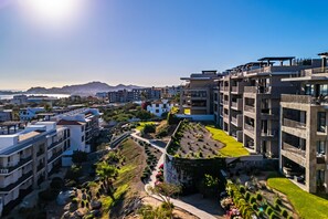 Un paysage urbain moderne avec des immeubles à plusieurs étages, un jardin aménagé et une chaîne de montagnes visible au loin.
