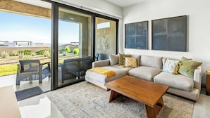 A modern living room with a sofa, coffee table, and a sliding glass door leading to a balcony. - Modern Apartment With Ocean View, Pool, Patio, Tennis & Gym (Cabo San Lucas)