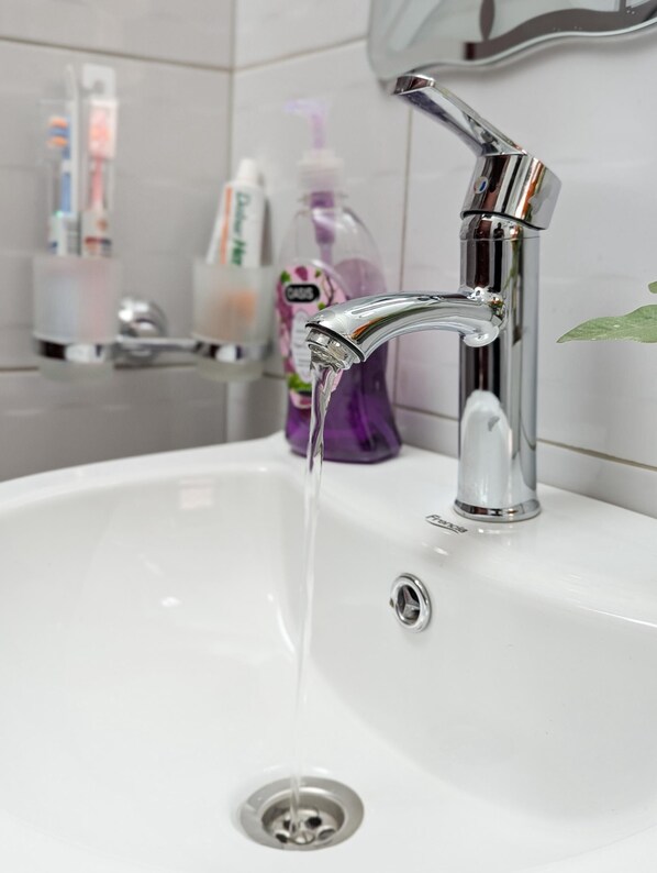 Un lavabo de salle de bain avec un robinet chromé, un miroir au-dessus et des articles de toilette rangés sur une étagère.
