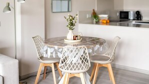 Un coin repas avec une table ronde, quatre chaises, un luminaire suspendu et une cuisine en arrière-plan.