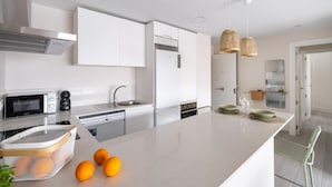 Une cuisine moderne avec des meubles blancs, un four encastré, un four à micro-ondes et un évier. Il y a trois oranges sur le comptoir.