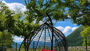 Un fauteuil suspendu avec un coussin rouge, dans un jardin offrant une vue sur une montagne.