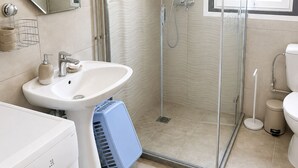 Une salle de bain avec une douche à parois de verre, un lavabo, des toilettes et un lave-linge.