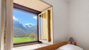 Une chambre à coucher avec un lit, une table de chevet, une lampe et une fenêtre donnant sur les montagnes.