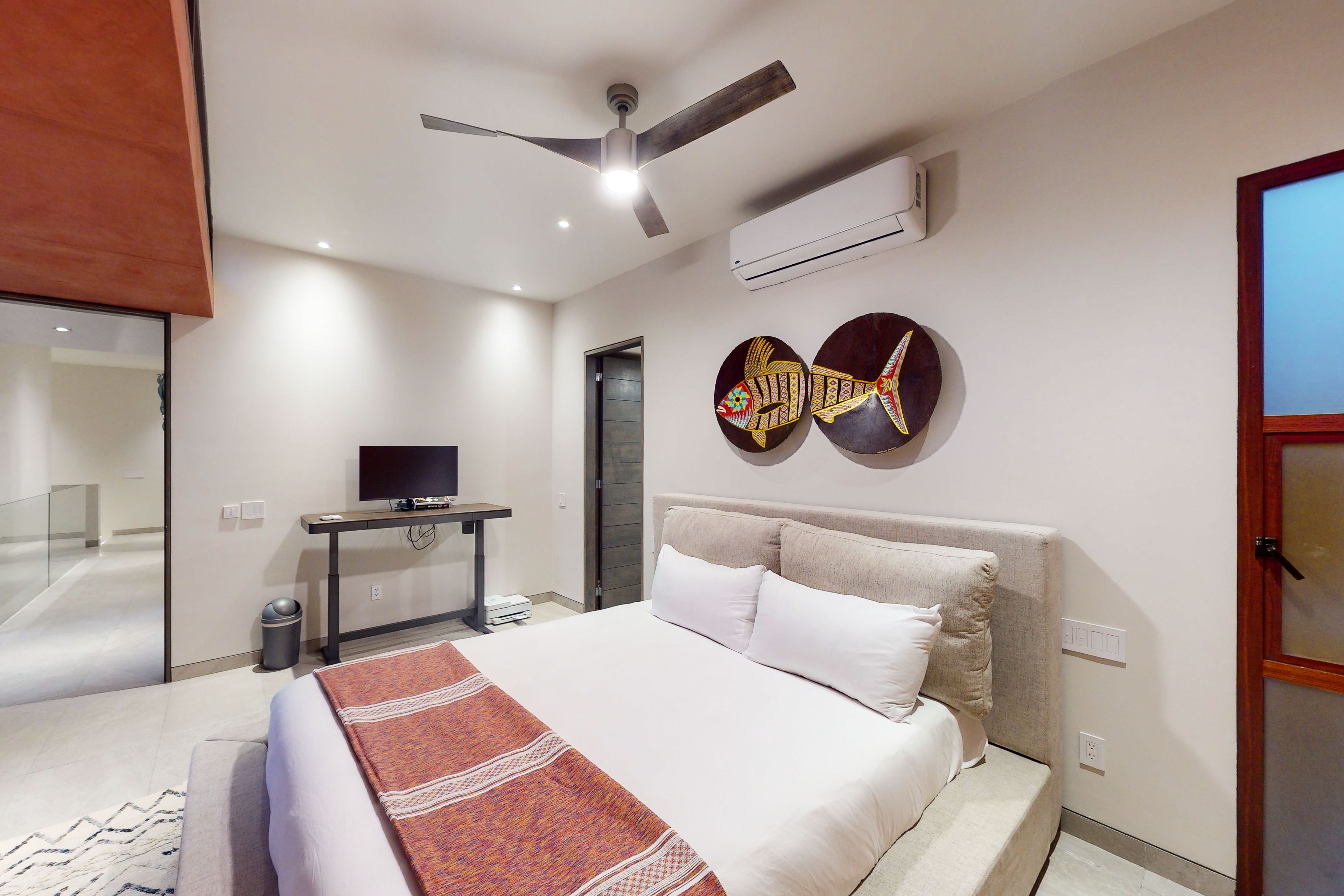 Ein modernes Hotelzimmer mit einem Bett, einem Deckenventilator, einer Klimaanlage, einem Fernseher und Kunstwerken an der Wand.