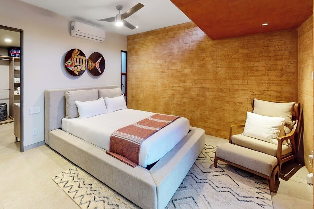 Ein modernes Schlafzimmer mit einem großen Bett, einem Sessel, einem Deckenventilator und einer Wand mit Holzverkleidung.