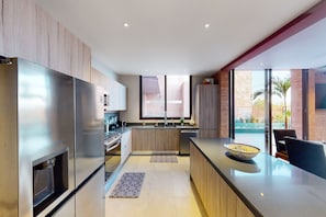 A modern kitchen with stainless steel appliances, wooden cabinets, and a large island with a bowl. - Luxury House With Private Pool, Ocean View, Inviting Balcony & Elegant Charm (San José del Cabo)