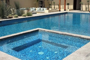 Ein Schwimmbad mit gefliestem Boden, umgeben von einer Lounge mit einer Couch und Topfpflanzen.