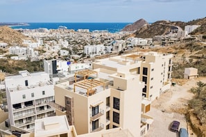 Ein Küstenwohngebiet mit modernen Gebäuden, freiem Blick auf das Meer und einer hügeligen Landschaft im Hintergrund.