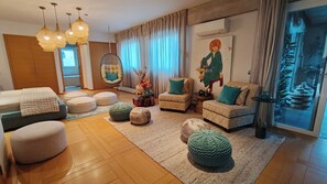 Ein modernes Wohnzimmer mit einer Couch, Hocker, einem Hängesessel und einem großen Fenster mit Vorhängen.