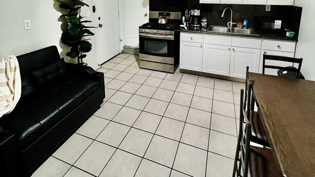 Un ambiente compatto con angolo cottura, ventola a soffitto, tavolo da pranzo e divano nero.